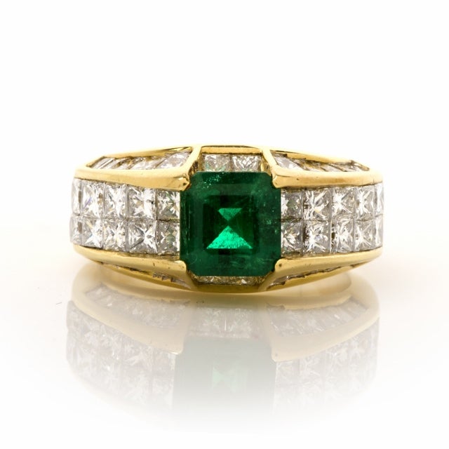 This exquisite emerald and diamond engagement ring of European design and craftsmanship is constructed in 18K yellow gold, weighs 10.1 grams and measures 10mm wide and 5mm high. With an  alluringly sophisticated  design of steep, elevated gallery,
