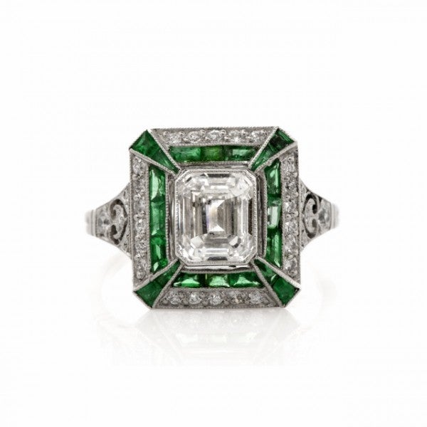 This Art Deco inspired engagement ring with diamonds and emeralds is crafted in solid platinum and weighs approx. 4.8 grams. Designed as a rectangular plaque measuring 20mm x 16mm, this alluring ring of enchanting aesthetic is centered with a