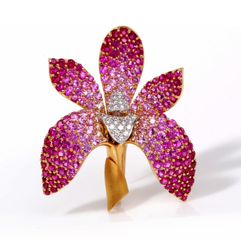 This stunning designer Mark Patterson estate floral brooch pin from the Intensity Collection, is crafted in solid 18k yellow gold and platinum.  This orchid floral pin is accented with some 104 pink sapphires approx. 10.00ct. in various hues. The