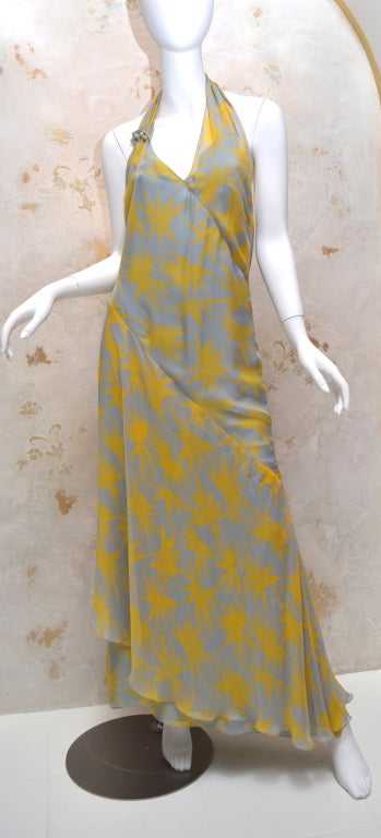 Chanel bias cut chiffon halter gown from the 2000 cruise season. Gown has a yellow starburst print pattern with CC logo printed in the middle on gray background. Bias cut panels and layered chiffon allow dress to gently skim the body. Asymmetrical