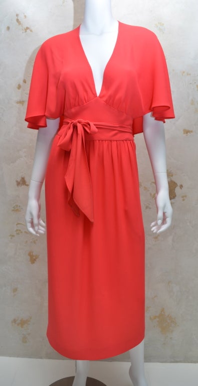 Halston 1970's tangerine lightweight crepe halter day dress with built in draped shawl collar. Dress has side hidden pockets in the skirt. Wrap around skirt allows for variation is size. Under bust flat waistband with tie belt. Gathered bust area