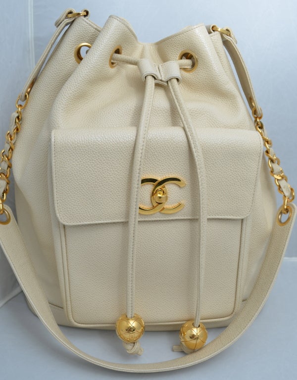 Chanel off white or cream extra large drawstring tote handbag with gold hardware, large gold CC logo, large gold balls with quilted pattern, and attached zipper pouch located in main compartment. Front pocket on the outside is large enough for a