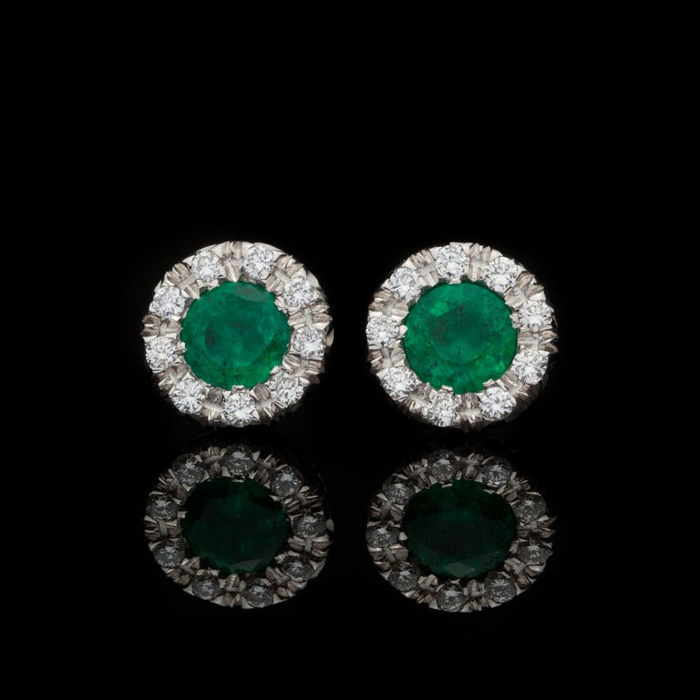 Favero Emerald and Diamond Stud Earrings, set in 18Kt White Gold, feature 2 Round Cut Emeralds for approximately 0.88cts accented by 20 round diamonds set halo style for a total of approximately 0.20cts.  Earrings weigh 2.43 grams, and measure 8mm