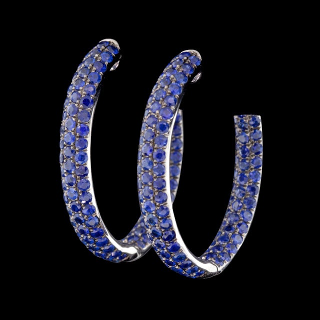 18Kt White Gold hoop style earrings with approximately 6.50cts of Round Brilliant Cut Sapphires. The earrings measure 5mm wide, 31mm in diameter, and weigh 12.5 grams.