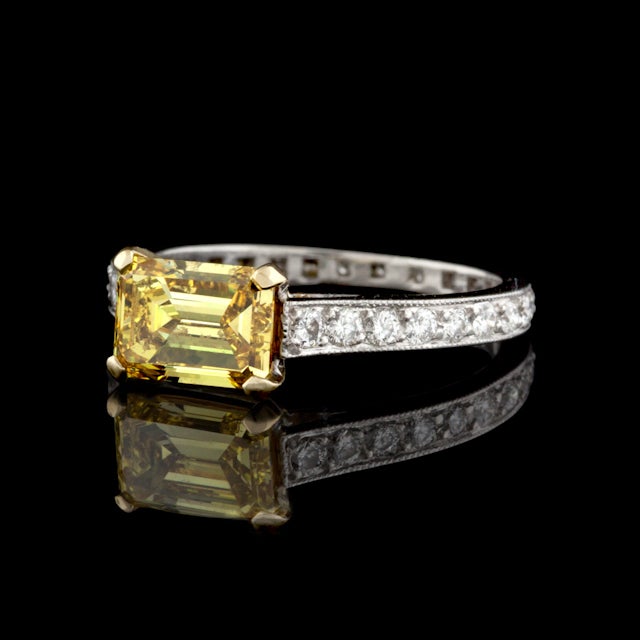 Graff Ring features a Natural Fancy Vivid Yellow Emerald Cut Diamond weighing approximately 1.34cts accented by 28 Round Brilliant Cut Diamonds for a total approximate weight of 0.34cts set in Platinum.  Total weight of the ring is 3.1 grams.  GIA