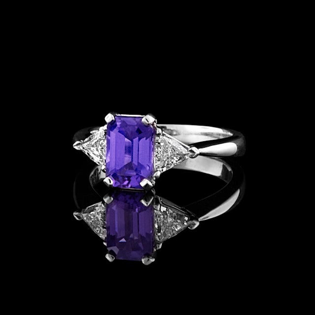 Platinum ring features one 2.05ct Emerald Cut Purple Sapphire with 2 Triangular Cut Diamonds with a total approximate weight of 0.67cts.  The total weight of the ring is 6.4 grams.
