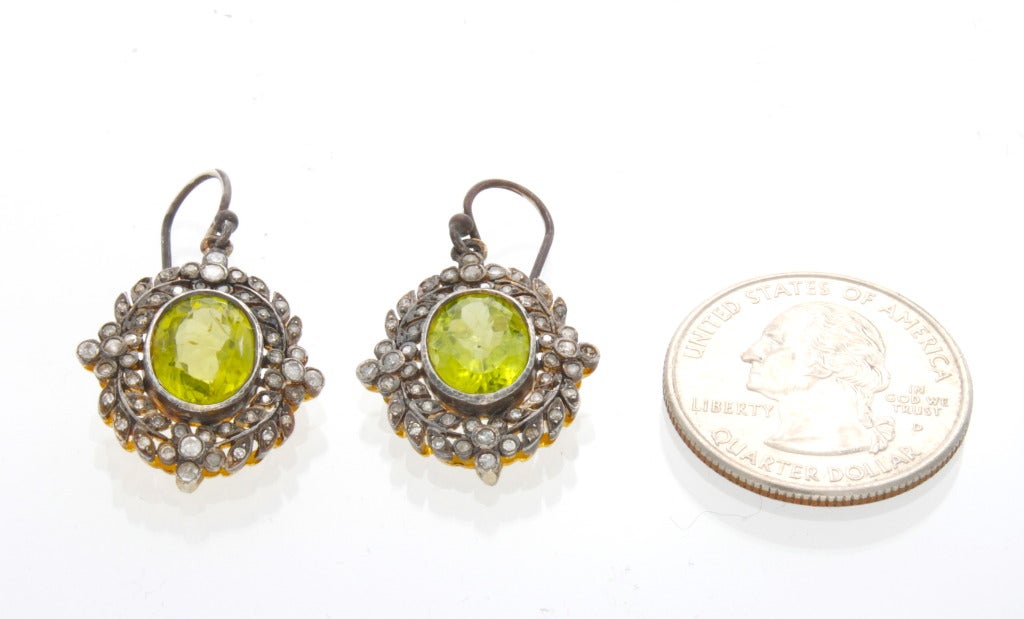 A pair of antique style silver earrings made in the Edwardian style backed by vermeil each centering an oval faceted peridot weighing approximately 2.50cts and further surrounded by fifty rose cut and round diamonds bordered in a wreath motif and