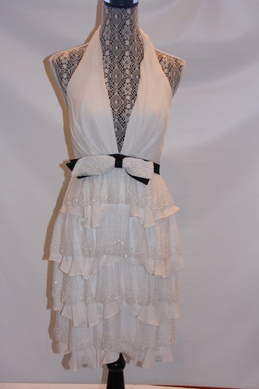Classic little cocktail gown in off white with black waistband. Halter style top with plunging back. Four layers of scallops trimmed in almost clear beads. Designer label.