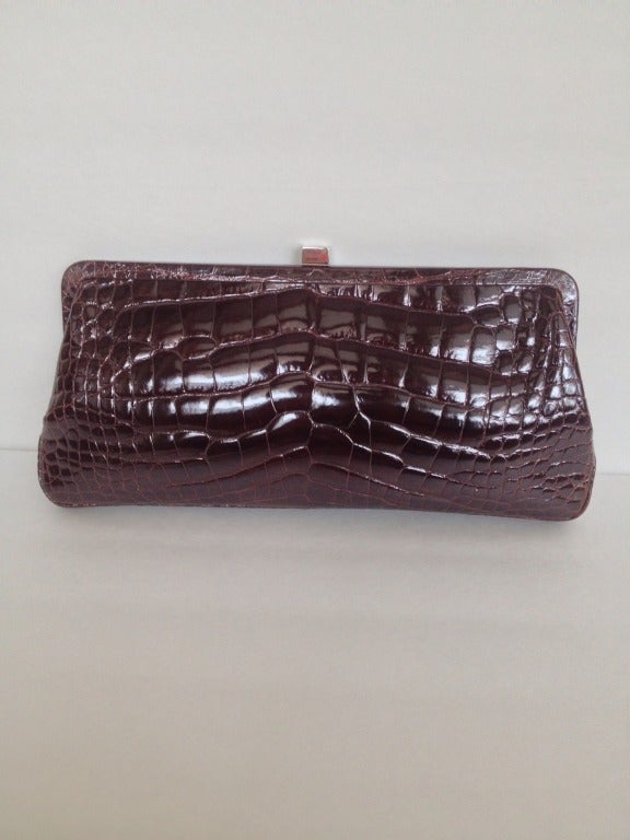 Serious beauty. 

This impeccable clutch is made with genuine alligator, with a deep patent finish the color of cherry chocolate. The structured body closes with a silver clasp and is lined with cloud gray suede, containing a single interior zip