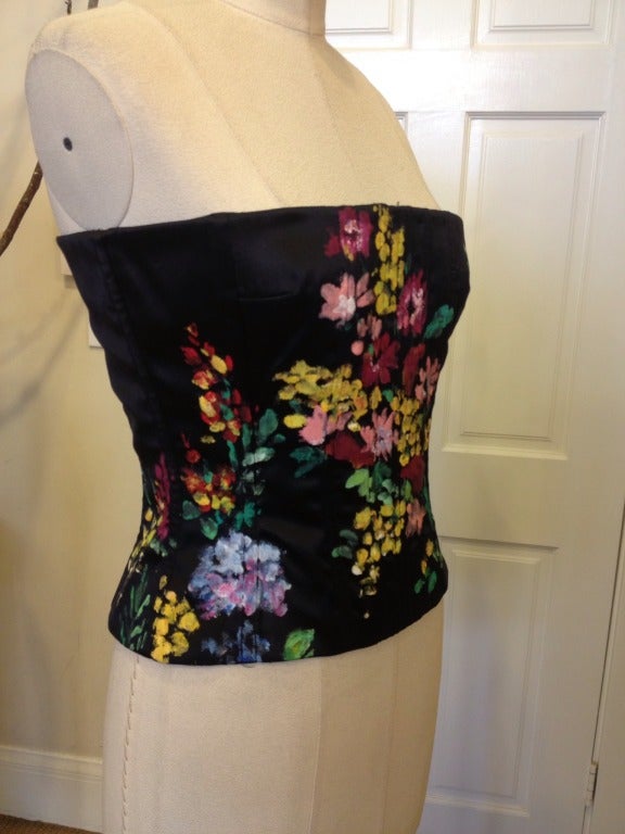 A fresh take on the classic bustier, vibrant yellow, pinks, green and blue make up the floral scenery.  Thick black silk contrasts the colors which are hand painted onto the fabric.  Boning contours the torso for a gorgeous silhouette.  Hook and eye