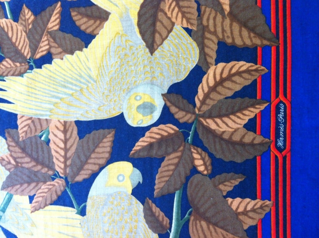 This beautiful Hermes scarf features seven yellow parakeets in various poses on a vine among brown and coral leaves. This design sits upon a navy blue ground, with a multi-linear red border on royal blue. While cheerful and tropical, the aesthetic
