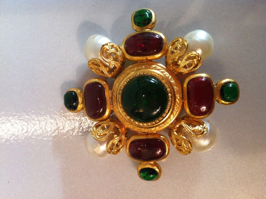 This dramatic Chanel brooch features vibrant green and fuschia-red gripoix stones set in gold-colored metal.  Four pearls accent the diagonals with a pin backing. This brooch will create a statement on every lapel, whether alone or anchoring a
