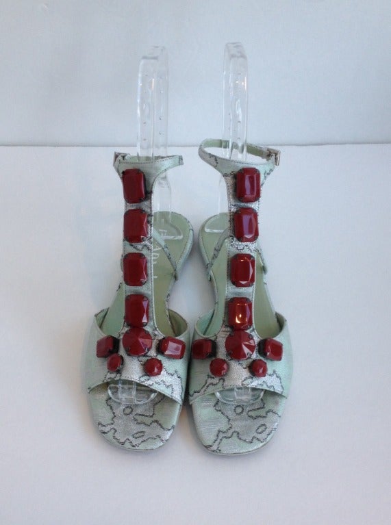 Treat your feet to a little shimmer with these delightful Prada T-strap sandals! The outer fabric is a beautiful light pistachio green and silver brocade accented with brick red jewel-like beads along the vamp of the shoe. The inner lining is a