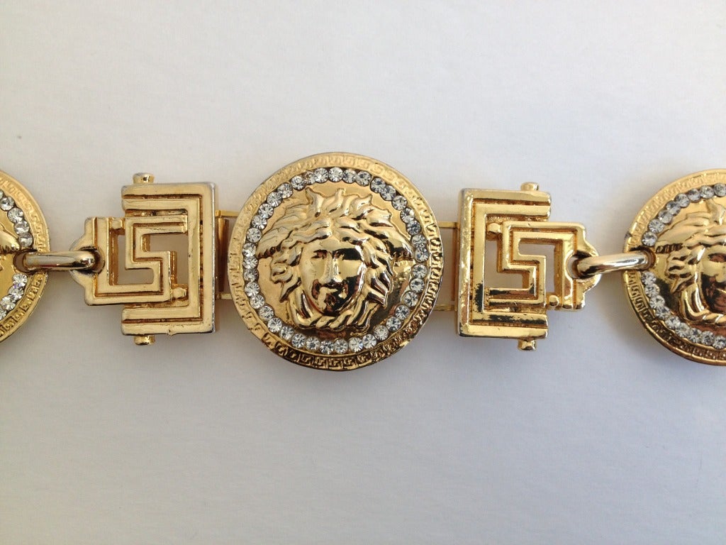 Look like royalty in this iconic bracelet by Versace.  Shiny, gold colored metal has 3 coin-like medallions edged with beautiful, sparkly rhinestones.  Each coin has the head of Medusa depicted.  The clasp has a similar coin in a smaller version. 