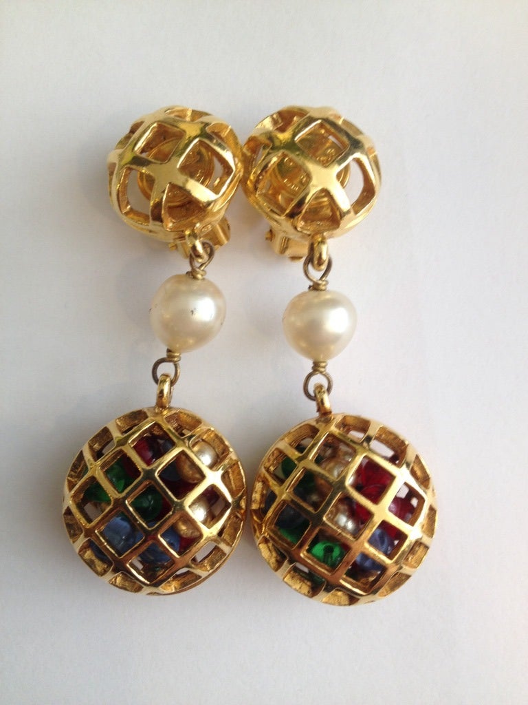 These Chanel clip on earrings are simply stunning! They empty gold cage sits on the earlobe, with a hanging pearl and another cage filled with red, blue, green, and gold beads floating freely. The Chanel stamp on the inside of the first cage shows