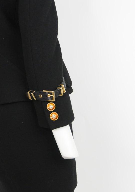 Black wool 2pc suit with enamel and rhinestone buttons. Leather straps with gold buckles at front closure and gold metal tabs on collar and pocket details.
