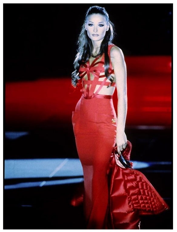 Fire red long maxi bondage dress. Heavy strap and buckle detail adorn bodice of this iconic gown. The skirt is fitted through the hips with two large patch pockets and a long slit at back seam.