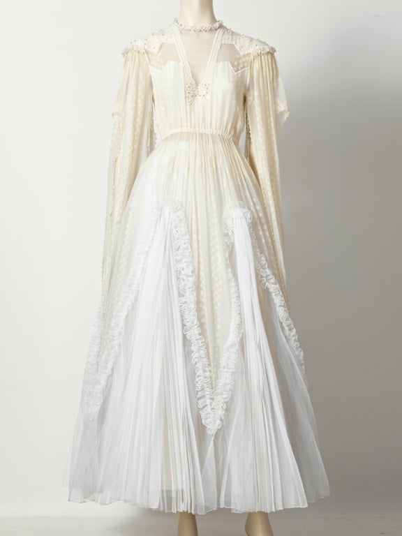 Zandra Rhodes, custom made wedding dress C. 1982.Painted , ivory and white chiffon with tiny seed pearl embellishment. Crystal pleated triangular panels with ruffles. Long pointed panels extend from shoulders edged in seed pearls and drop down the