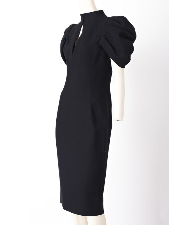 Alexander McQueen, black wool crepe fitted dress with pleated,
sculpted sleeves that angle at the upper arm. Neckline is high and fastens with hook and eyes with a peep hole in the center front showing the decolte.