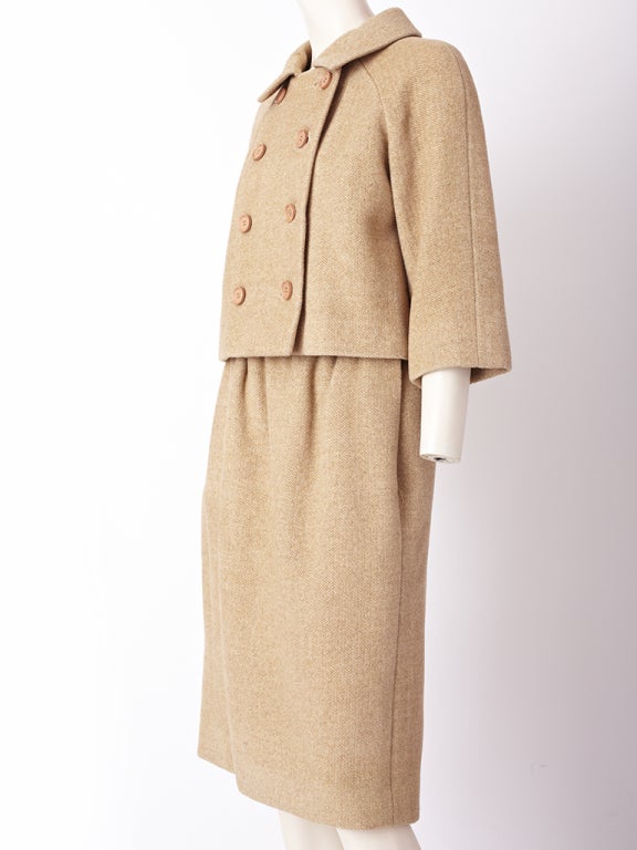 Norell, camel tone, brushed wool suit with a subtle herringbone pattern.
Jacket is double breasted, with a raglan sleeve , falling at the hip.
Skirt has slight gathering at the waist with a straight silhouette.
