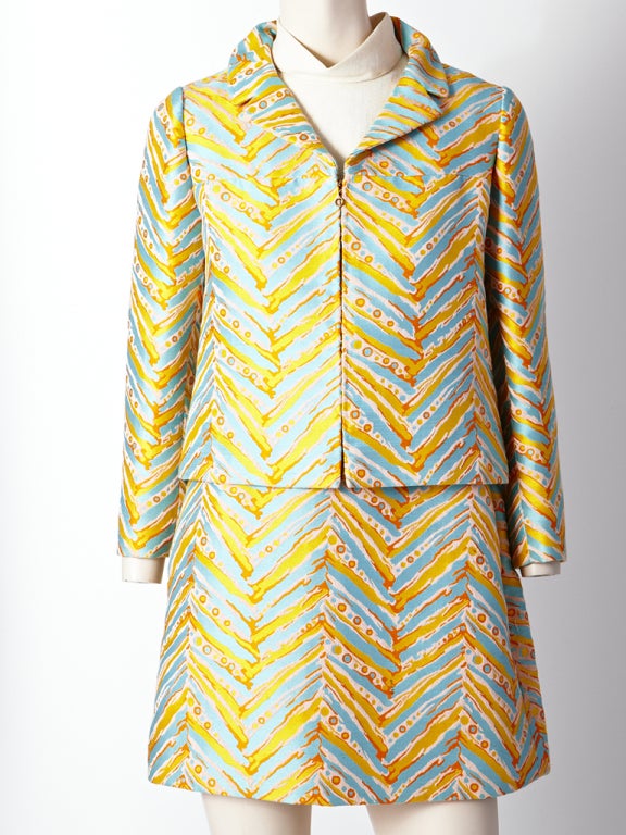 T. Jones, turquoise and orange abstract, chevron pattern print dress and jacket. Fabric is tapestry like.Jacket has a front zipper closure with a notched collar. Dress is sleeveless, with  and ivory linen bodice and self belt with a mother of pearl