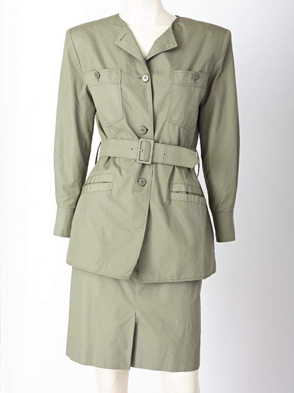 Courreges, c. 1980's olive green, cotton, Safari style, suit.
The jacket is collarless, belted, with breast pockets and ends just at the thigh. Skirt is slim fitting with a kick pleat in the front.