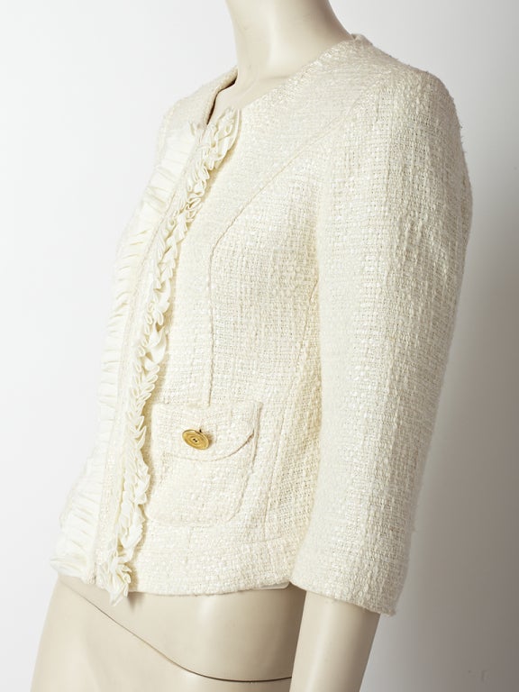 Chanel, ivory tweed jacket with 3/4 sleeves, hook and eye closures, ruffle detail down the front and two small pockets above the hip with gold Chanel buttons. Jacket ends above the hip
and is slightly fitted.
