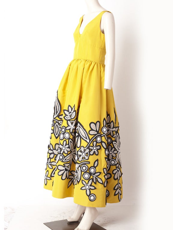 Oscar de la Renta, Chrome yellow, taffeta, appliqued, gown.
Bodice is fitted with a v neck line. Skirt is gathered, with pockets and embellished with black taffeta and white embroidered floral motif,appliques, creating a graphic effect.