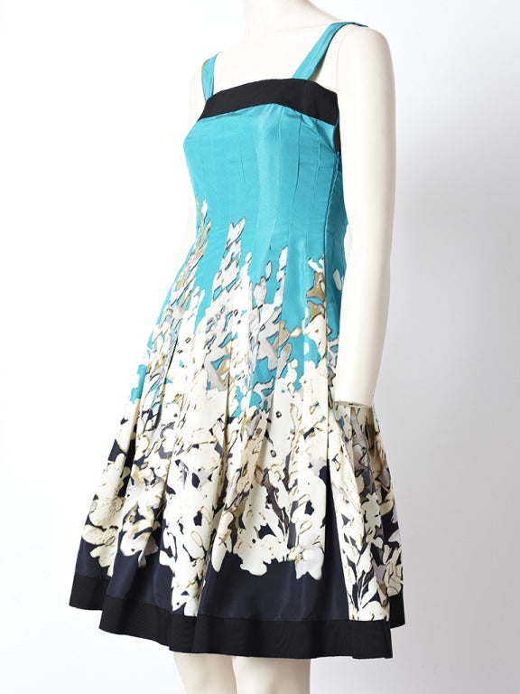 Oscar de la Renta, turquoise and black, taffeta cocktail dress with a fitted bodice and stitched down hips. Box pleats start at the hip and go to hem. Black gross grain band at the hip and hem. Abstract, floral motif pattern.