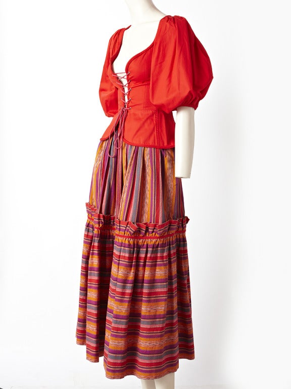 Yves Saint Laurent, 2 piece gypsy ensemble from the late 70's. Top is a red heavy cotton with lace up front and full sleeves trimmed in a cotton braid.
Skirt is a multicolored, Indian woven cotton stripe, that is gathered at the waist with a tier