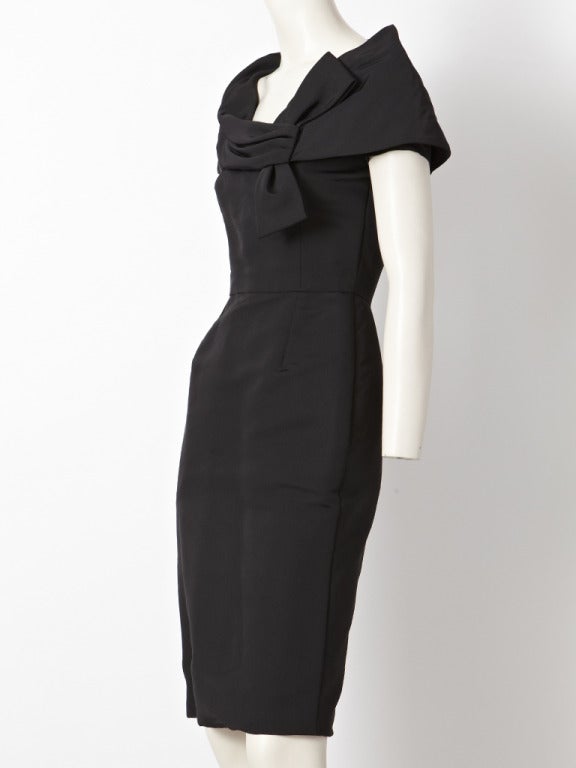 Bill Blass, taffeta, faille, 1950's inspired cocktail, dress. Bodice is fitted with a cape like shoulder and sleeve treatment. Front is slightly draped with a knotted 
bow embellishment off the left shoulder. Skirt of dess is straight.