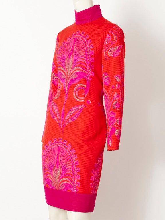 Versace, ribbed fitted dress with turtleneck. Background of dress is red, with a magenta turtleneck and hem. Dress has a pattern that is symmetrically placed in the center , sides sleeves and back. The pattern has shades of hot pink and Magenta with