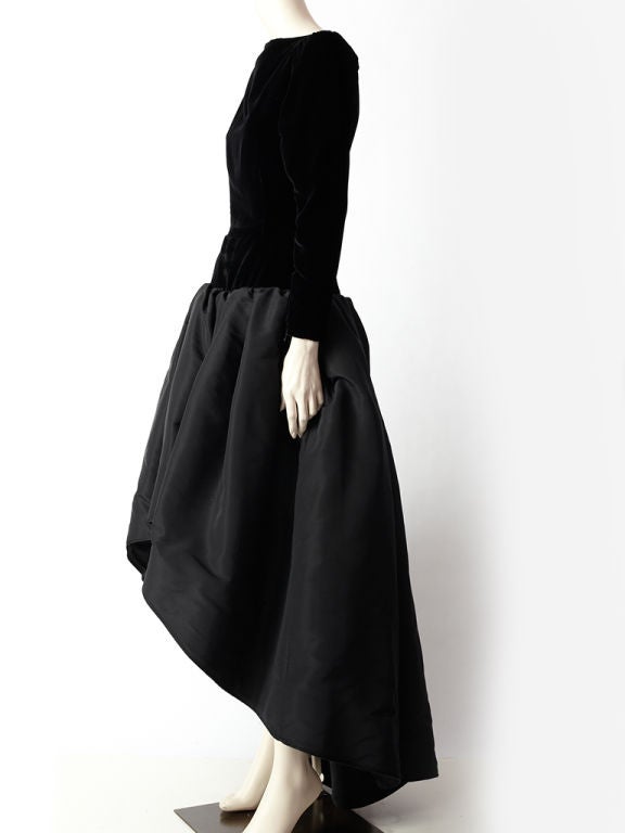 Yves St. Laurent evening gown made of a velvet bodice and taffeta<br />
skirt. Bodice is boat neckline with long slim sleeves, fitted and ends at the hip. ( dropped waist). Skirt is full and made of a backed taffeta, which is shorter in the front