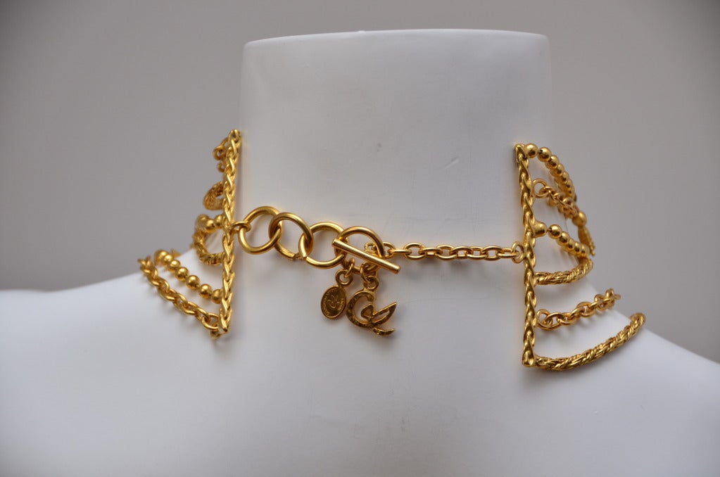 Collar necklace in gold tone.6 tiered alternating chains in 3 different styles: Ball Chains, Link Chains and Twisted Chains.
The chains are held by 4 rigid textured space bars.
Variety of Christian Lacroix's iconic charms are dangling randomly: