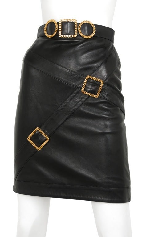 Soft black lambskin pencil skirt with gold tone belt buckle and strap detail. Snap and zip closure at back.