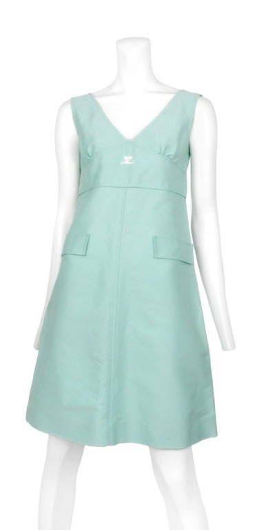 IVintage Andre Courreges mint green cotton sleeveless shift dress featuring a v neck, empire waist line, center seam, two front pockets, double button closure in back and white Courreges logo at neck line. Few faint spots on the bust as well as the