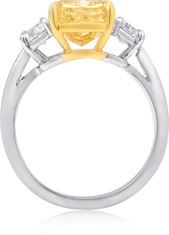 Three stone engagement ring, 4.01 carat Cushion-cut Fancy Intense Yellow color diamond GIA certified VVS2 clarity, 0.97 carat Trapezoid-cut diamonds. Set in platinum and 18k yellow gold.