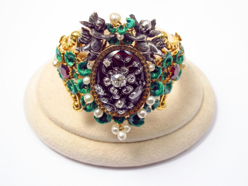 An antique enamelled yellow gold bangle with garnets, rose-cut diamonds and natural pearls. The center, with silver Puttis, can be transformed into a pendant. France, 1850. Attributed to Jules Wièse. A very similar bangle with is in the collection