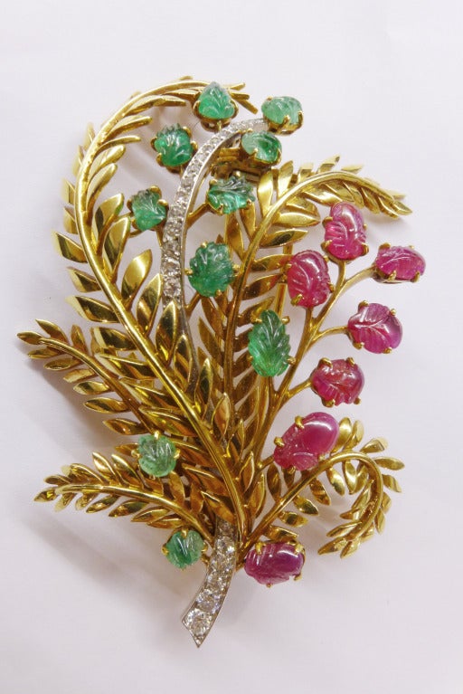 A Chaumet yellow gold broach representing a bundle set with brilliant-cut diamonds on the platinum stems, engraved emeralds and rubies on the leaves. 
Height : 73 mm 
Width : 45 mm 
Circa 1950-1960