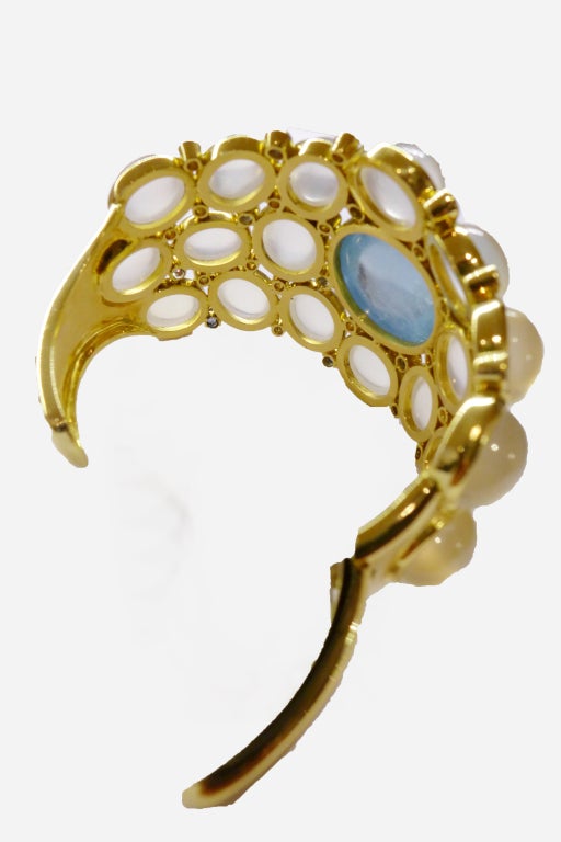 A yellow gold very spectacular Temple Saint Clair cuff-bracelet set with a magnificent cabochon cut aquamarine weighting about 25 carats and on both sides of it, cabochon royal blue moonstones, sapphires and diamonds.  Hinged on one side.
Central
