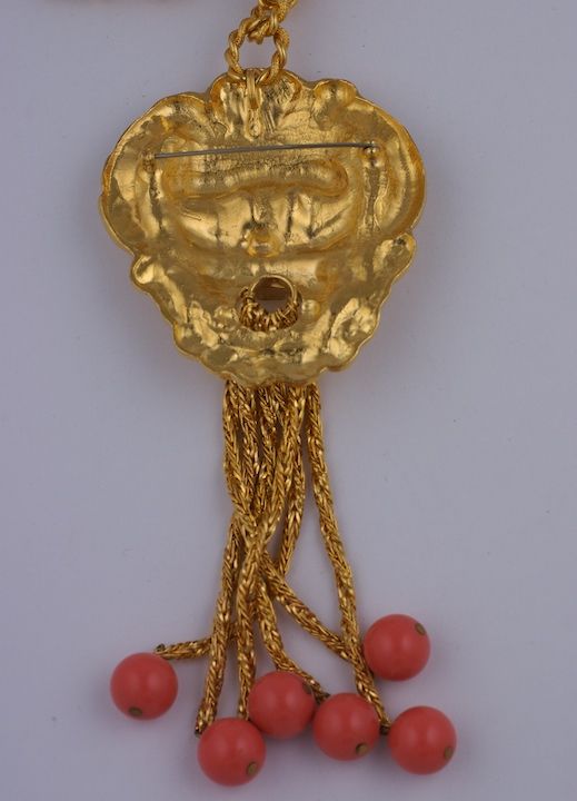 Vergoldeter figuraler Anhänger mit Quaste und korallenfarbenen Perlen. Vergoldete, gedrehte Seilkette, Anhänger auch mit Anstecknadel erhältlich. USA 1980er Jahre.<br />
Ausgezeichneter Zustand.