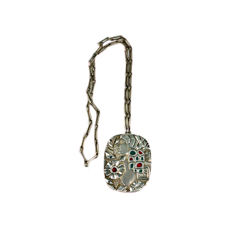 Joli pendentif en sterling et émail dans le style sécessionniste des années 1970. Fleurs et coiffe émaillées en rouge brûlé et turquoise profond. Repoussé de l'arrière et soutenu par une base en bakélite noire. Chaîne à maillons de sécurité martelée