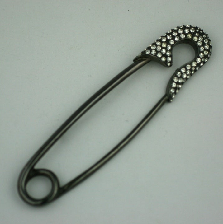 Oversized safety pin brooch set in blackened metal with pastes by Marla Buck. USA 1980s. Great for closing oversized sweaters. Safety Pin does not actually open, there is a pin mechanism behind it.
Excellent Condition. 5