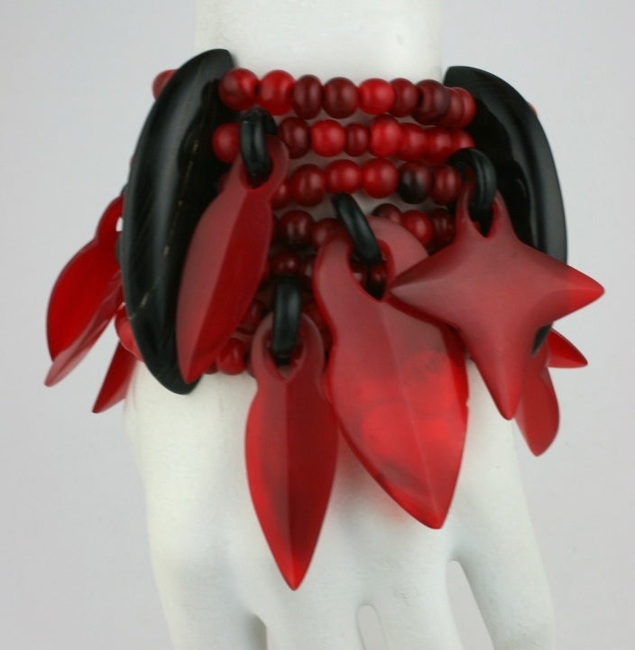 Monies resin charm cuff by Danish team of Gerda and Nicolai Monies of Denmark. Large spear and star shaped charms hang off the multi-row elasticized bracelet. Striking red and black combination. 1980s.<br />
Excellent condition.
