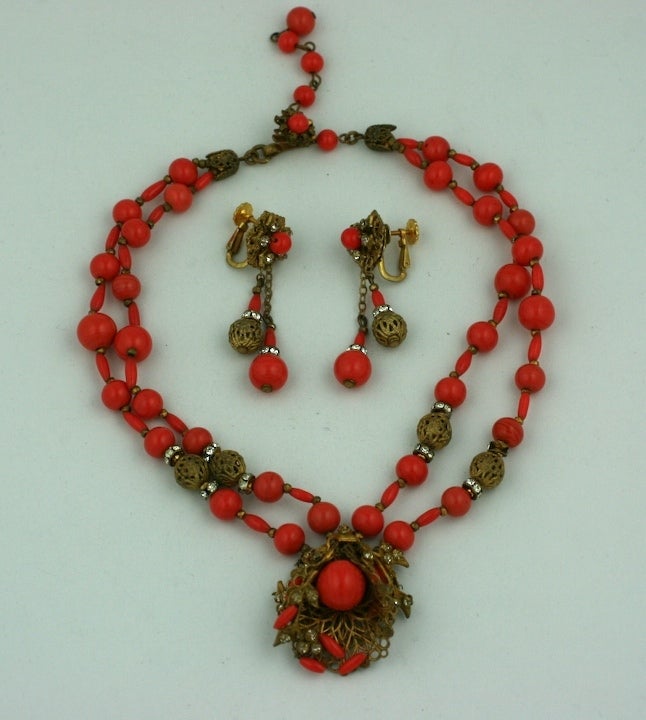 Suite de collier et de boucles d'oreilles en perles de pate de verre rouge corail Haskell mélangées avec des trouvailles et des pâtes filigranes dorées.<br />
Les boucles d'oreilles sont munies d'un clip réglable. années 1940, États-Unis.<br