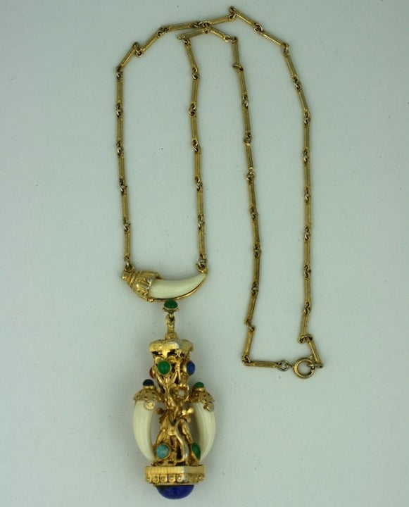 Unusual pendant of faux ivory tusks mounted in a baroque framework of gilded metal and semiprecious glass cabochons.
Primarily blue toned in front, the obverse has jade and carnelain cabochons.
American 1970's. 
Excellent condition.