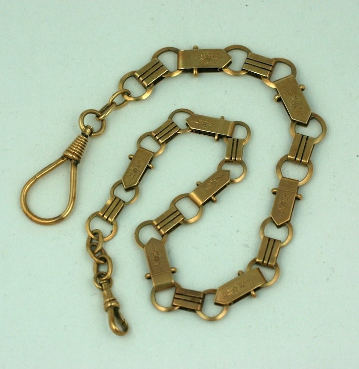 A victorian 14K gold watch chain worn with a watch on one end, carrying a fob on the other. Of gold round and two sizes of rectangular links, ribbed and etched in an aesthetic taste. Circa 1880. 13.5