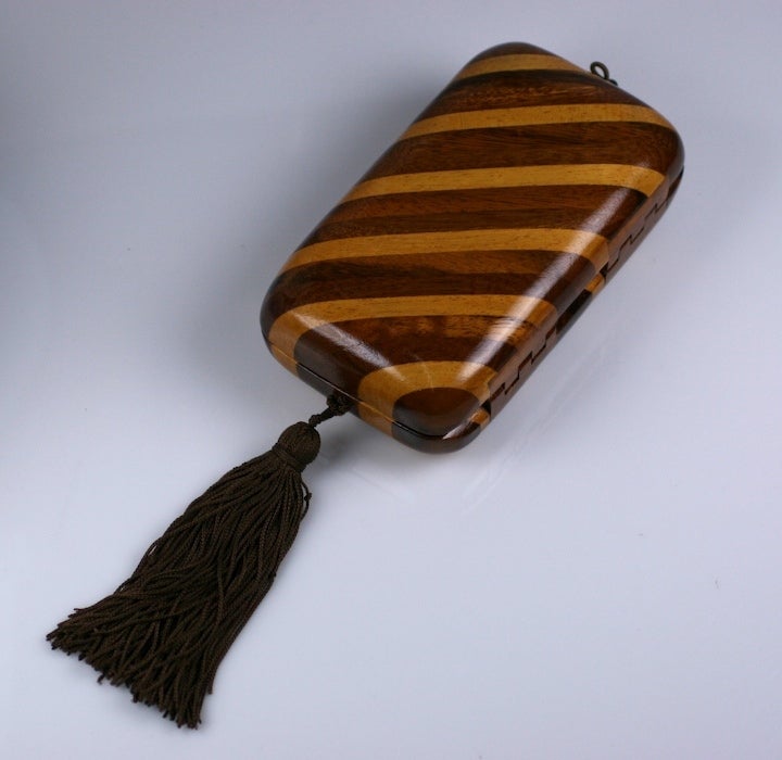 Raphael Sanchez's designs epitomized the vibrancy and glamour of the late 70's and early 80's. A black silk tassel hangs from a pieced wood minaudiere of exotic woods. Inside there is a black silk shoulder cord (retractable to use as a clutch) with