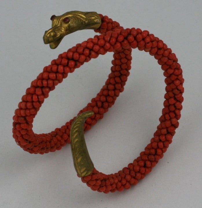 Extraordinary Victorian snake bracelet of genuine coral beads wired on a coiled metal core capped with finely detailed repousee gold filled snake head and tail. Head is set with rose cut faux ruby pastes stones. Beads have a lovely, rich coral