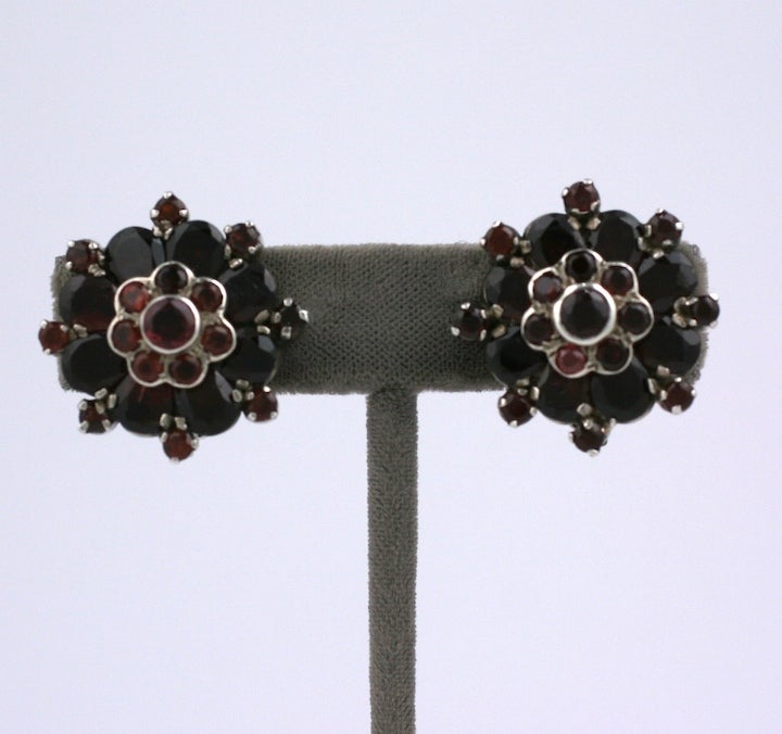 Dimensional garnet earrings in the shape of flower clusters with pear shaped and round garnets. Rich claret colored garnets set in heavy sterling silver mounts with clip back fittings. Elegant tiered design creates a 3D floral effect. 1